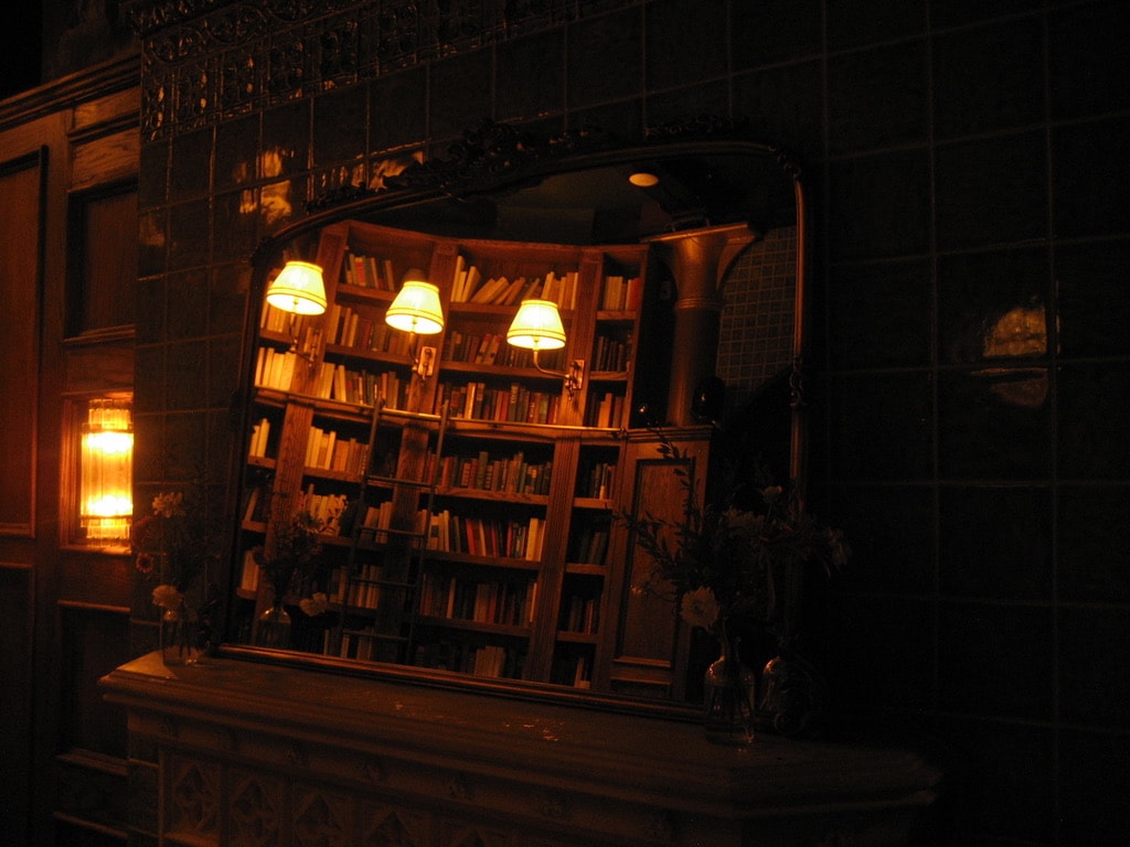 Lamplit bookshelves reflected in an ornate mirror